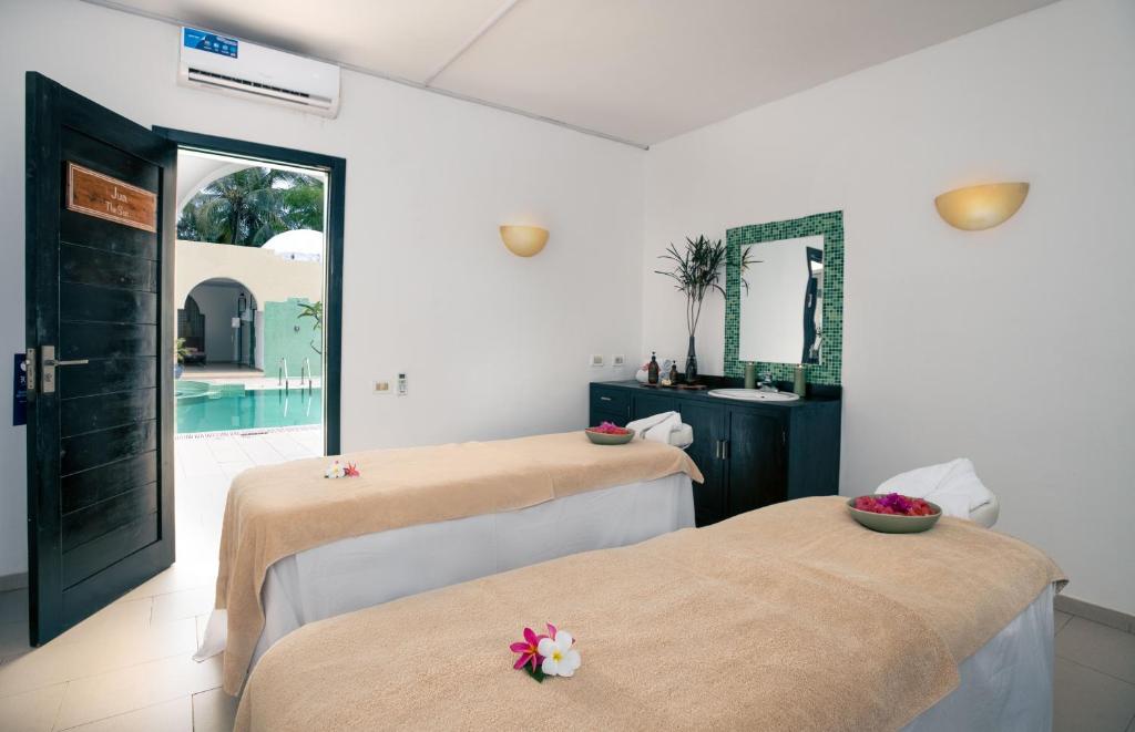 Spa telpa ar divām masāžas galdiem, ziedu dekorācijām un skatu uz baseinu caur atvērtām durvīm. Relaksējoša atmosfēra ar gaišām krāsām un dabas elementiem.