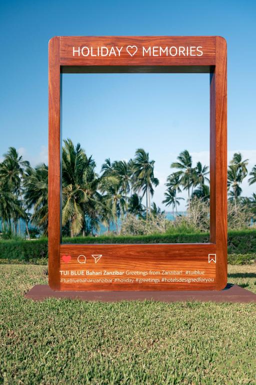 Koka rāmis ar uzrakstu "HOLIDAY ♥ MEMORIES", kas atrodas pludmalē ar palmām un jūras ainavu fonā. Ideāla vieta atmiņu iemūžināšanai.