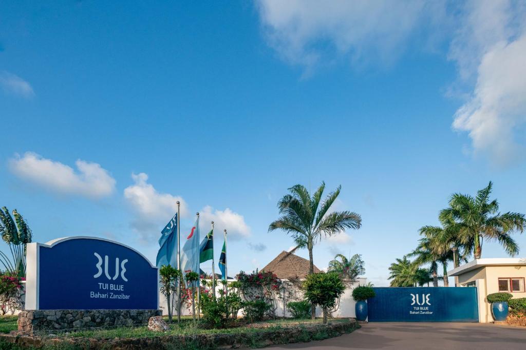 TUI BLUE Bahari Zanzibar viesnīcas ieeja ar karogiem un tropiskiem augiem, skaidras debesīs.