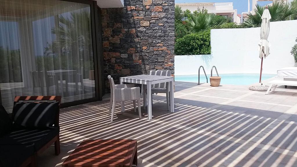 Mūsdienīga terase ar akmens sienu, galds un krēsli, kas nodrošina ērtu atpūtu, blakus baseins un saules gultas. Gaismas un ēnu spēle rada relaksējošu atmosfēru.