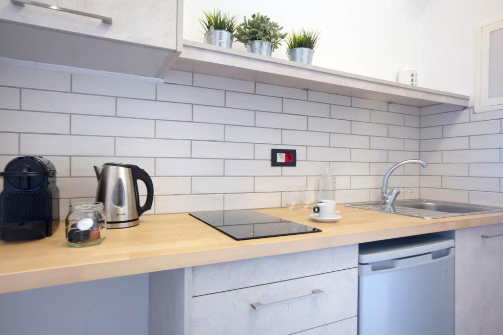 Mūsdienīga virtuve ar koka darba virsmu, elektrisko tējkannu un kafijas aparātu, kā arī augiem uz plauktiem. Virtuve ir izveidota ar gaišu flīžu apdari un modernu izskatu.