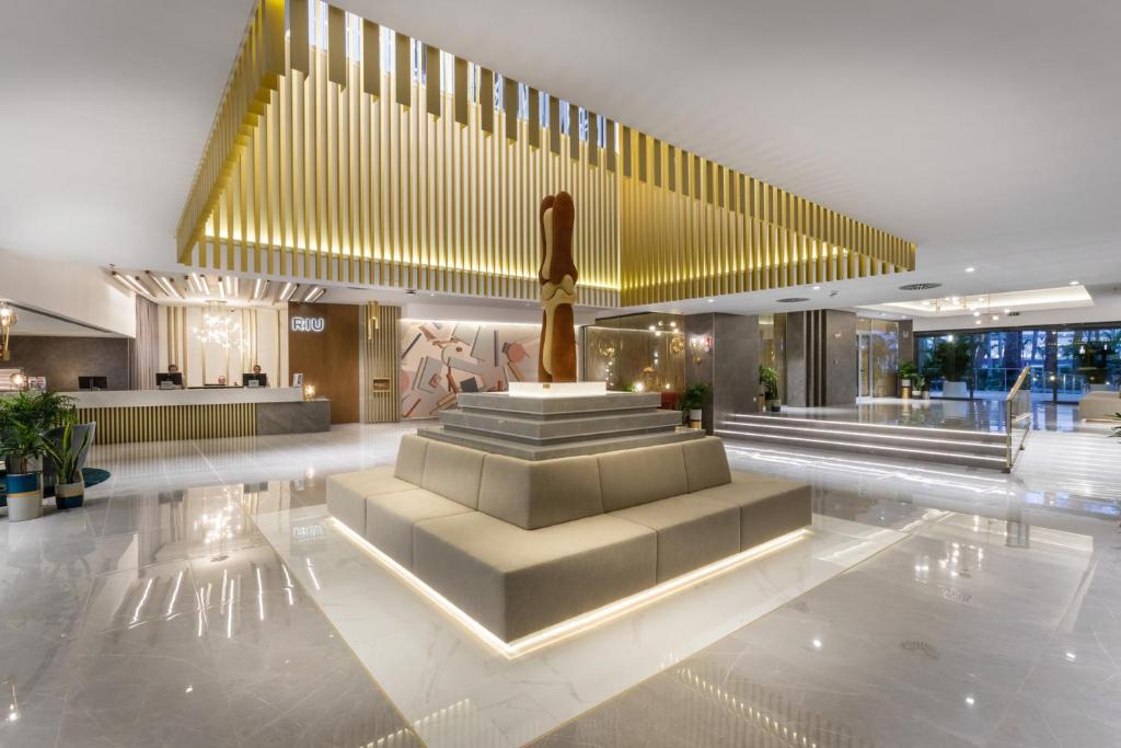 Mūsdienīgs viesnīcas reģistratūras interjers ar elegantu dizainu, centrā esošu skulptūru un modernām apgaismojuma detaļām. Ievērojami izmantotas neitrālas krāsas un augstas kvalitātes materiāli.