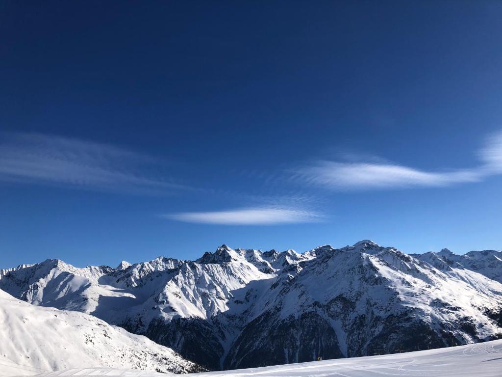 Sniegotu kalnu ainava ar skaidru zilo debesi un vieglām mākoņu svītrām. Ideāla vieta ziemas aktivitātēm un kalnu baudīšanai.