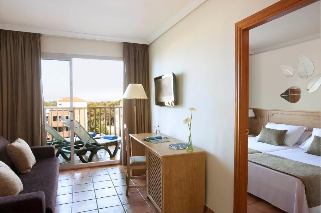 Mūsdienīgs viesnīcas numurs ar viesistabu un guļamistabu, lieliem logiem, kas ved uz balkonu, un ērtu mēbelējumu. Numurā ir televizors un galds ar ziedu kompozīciju.