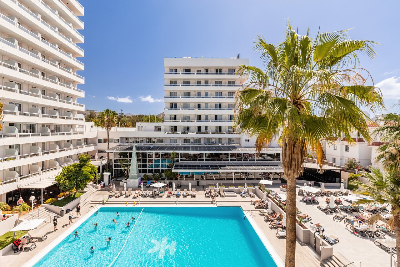 Viesnīcas komplekss ar baseinu un palmām, kas rada relaksējošu atmosfēru. Sauļošanās krēsli un viesi bauda atpūtu pie ūdens. panoramic view with beach and pools