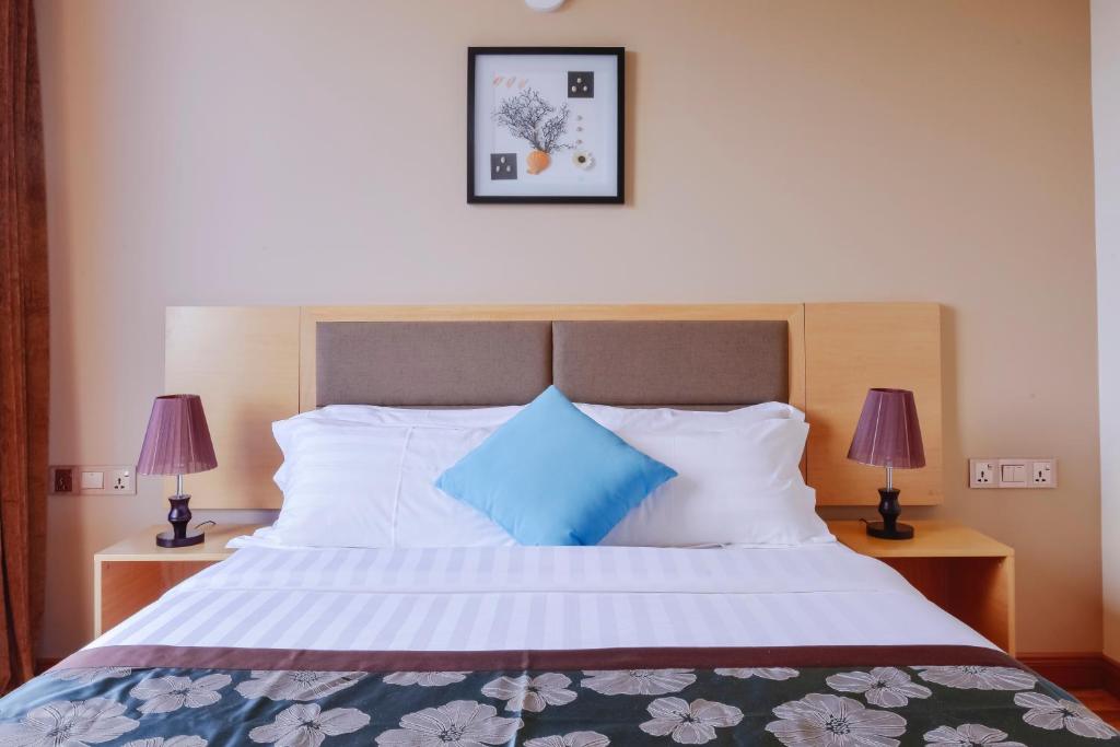 Mūsdienīga guļamistaba ar ērtu gultu, dekoratīvu spilvenu un naktslampām, papildināta ar mākslas darbu uz sienas.