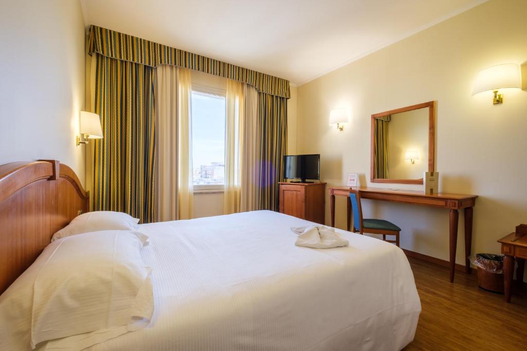 Mūsdienīgs viesnīcas numurs ar gultu, rakstāmgaldu un televizoru. Logā ieplūst dabiska gaisma, radot patīkamu atmosfēru.