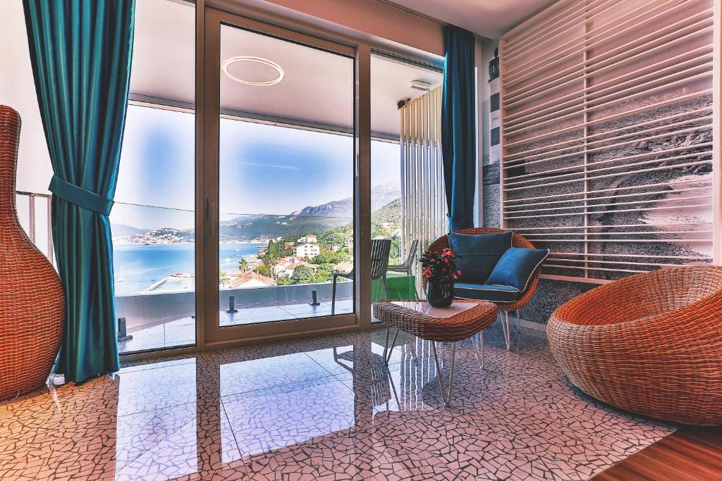 Mūsdienīgs interjers ar skatu uz jūru, kurā redzami vīnogulāju krēsli, galdiņš un tekstila akcenti. Lieliskas gaismas un krāsu kombinācijas, kas rada relaksējošu atmosfēru.