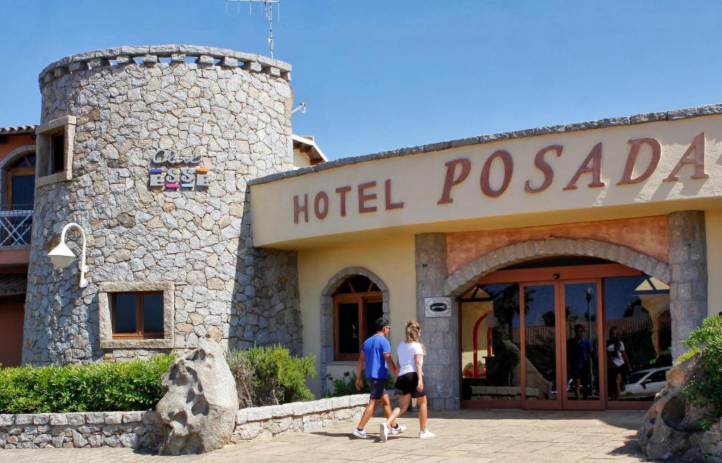 Viesnīcas "Posada" ieeja ar akmens sienām un diviem apmeklētājiem, kas ienāk iekšā. Redzama arī viesnīcas nosaukums uz ēkas.