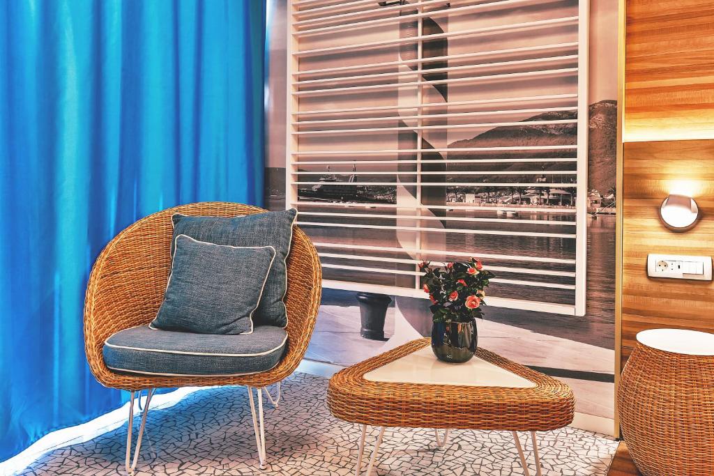 Mūsdienīgs atpūtas stūrītis ar vītnes krēslu, baltu trīsstūrveida galdiņu un zilu aizkaru, kas piešķir telpai svaigu izskatu. Uz galda atrodas ziedu pušķis, radot mājīgu atmosfēru.