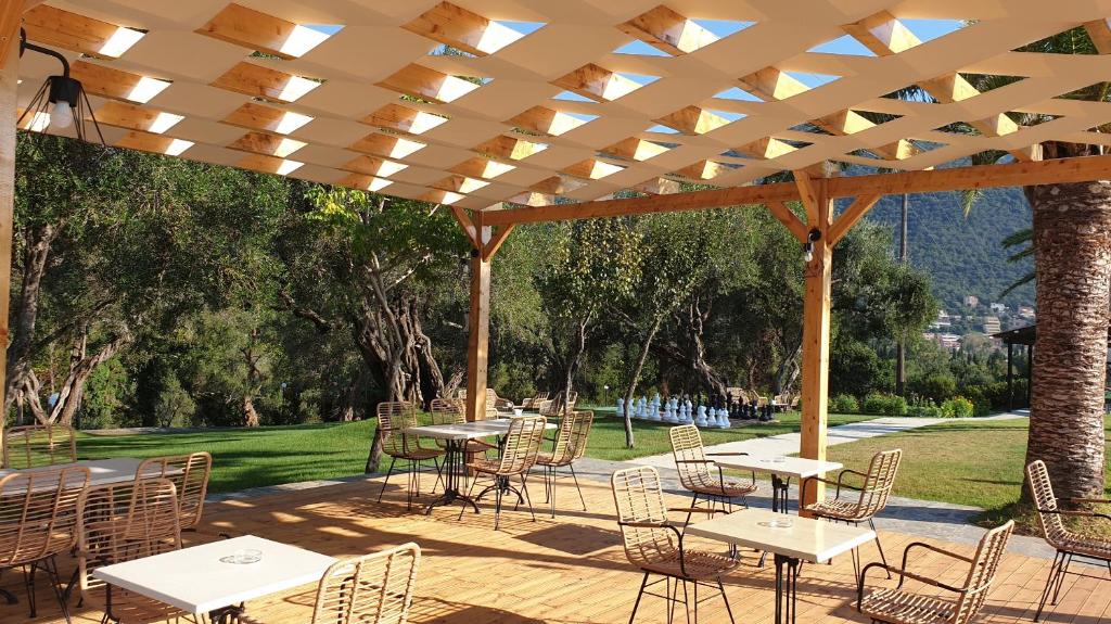 Āra kafejnīca ar koka nojumi, kurā ir galdi un krēsli, apkārt zaļa zāle un koki, radot relaksējošu atmosfēru. Ideāla vieta atpūtai un sociālām tikšanās reizēm.