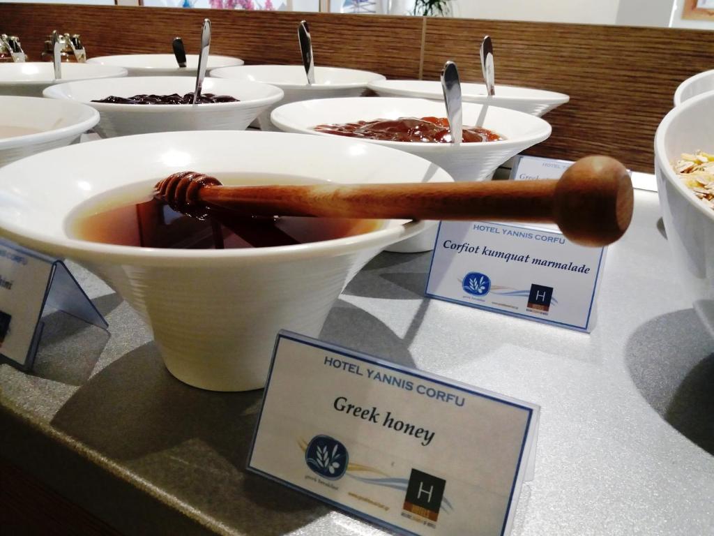 Trīs trauki ar dažādām ievārījuma un medus izvēlēm, tostarp Grieķu medus, viesnīcā Yannis Corfu, ar koka karoti medus trauciņā.