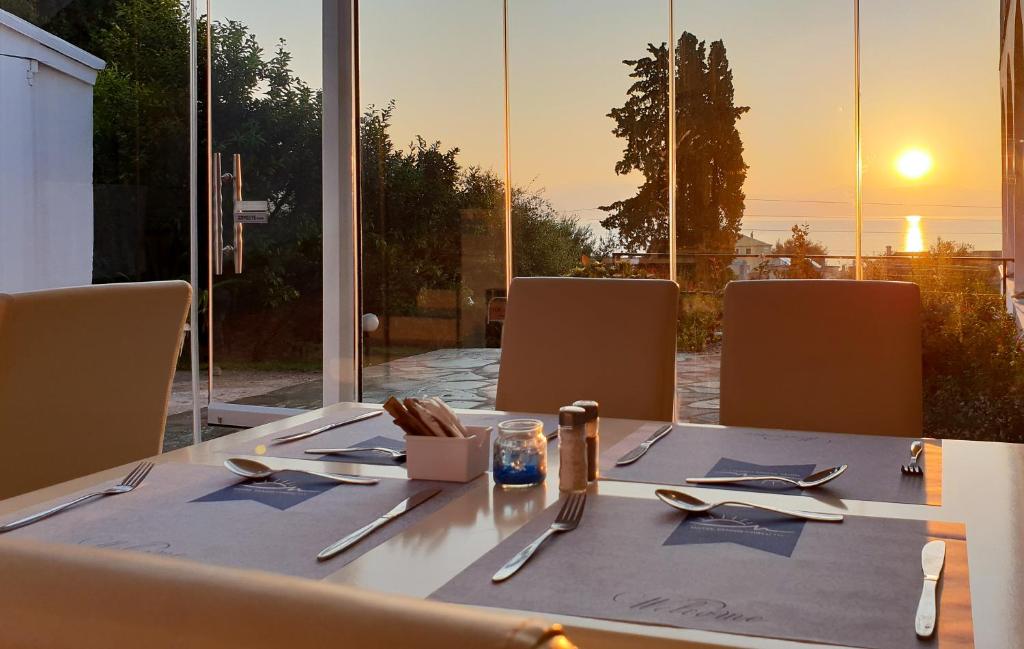 Saulrieta skats no modernā restorāna ar elegantām galdiem, kas gatavi viesiem. Caur stikla sienām redzamas ainavas un saulriets virs jūras.