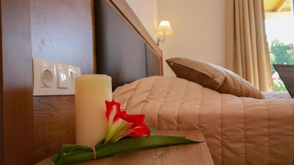 Mūsdienīgs guļamistabas interjers ar elegantu gultu, sveci un ziediem uz naktsgaldiņa, radot relaksējošu atmosfēru.