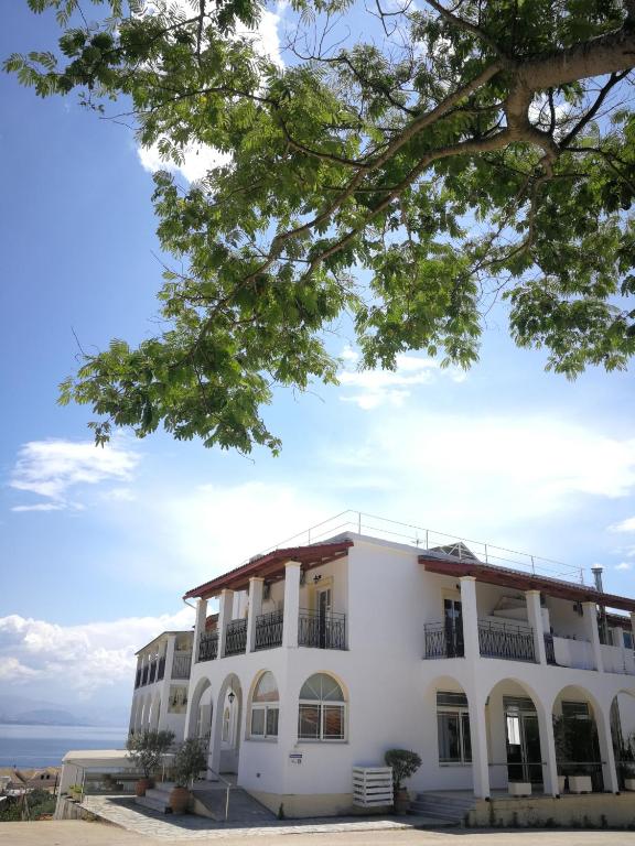 Moderns balts ēka ar arku logiem un sarkanu jumtu, ko ieskauj zaļa daba un zils debesis. Ideāla vieta atpūtai pie ūdens.