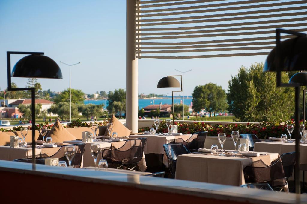 Restorāna terase ar elegantām galdiem un skatu uz ūdeni. Saulaina diena un zaļums rada patīkamu atmosfēru.