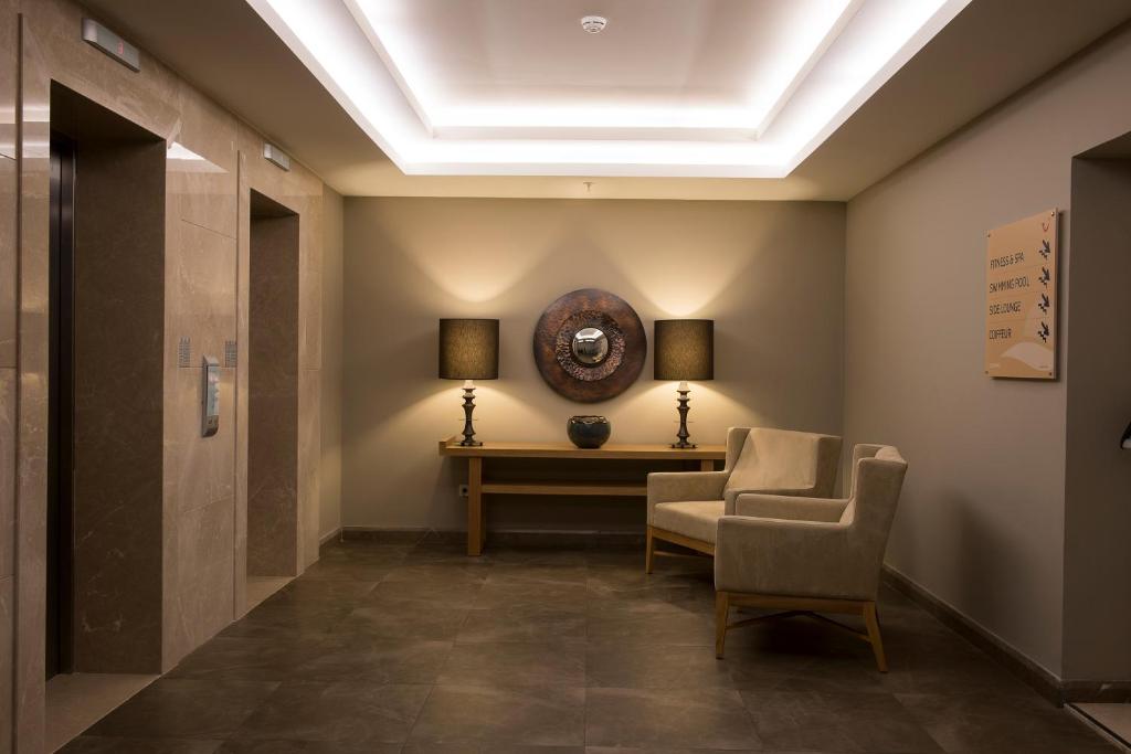 Mūsdienīgs viesnīcas vestibils ar liftu, elegantu lampu un stilīgu mēbeļu dizainu. Siltas krāsas un apgaismojums rada patīkamu atmosfēru.