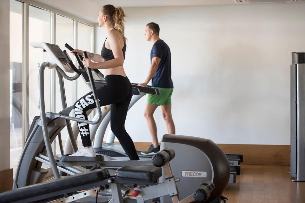 Divi cilvēki vingro sporta zālē, izmantojot kardio trenažierus, kas nodrošina aktīvu treniņu un veselīgu dzīvesveidu.