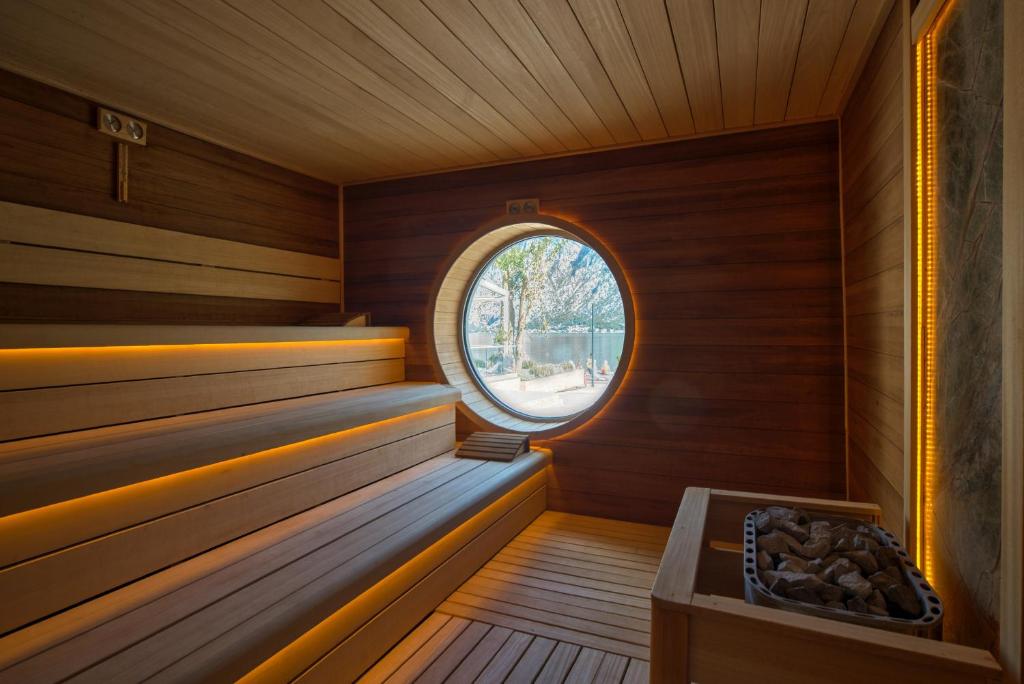 Mūsdienīga sauna ar koka apdari un ovālu logu, caur kuru redzams ārējais skats. Telpā ir izgaismotas koka plaukti, radot relaksējošu atmosfēru.
