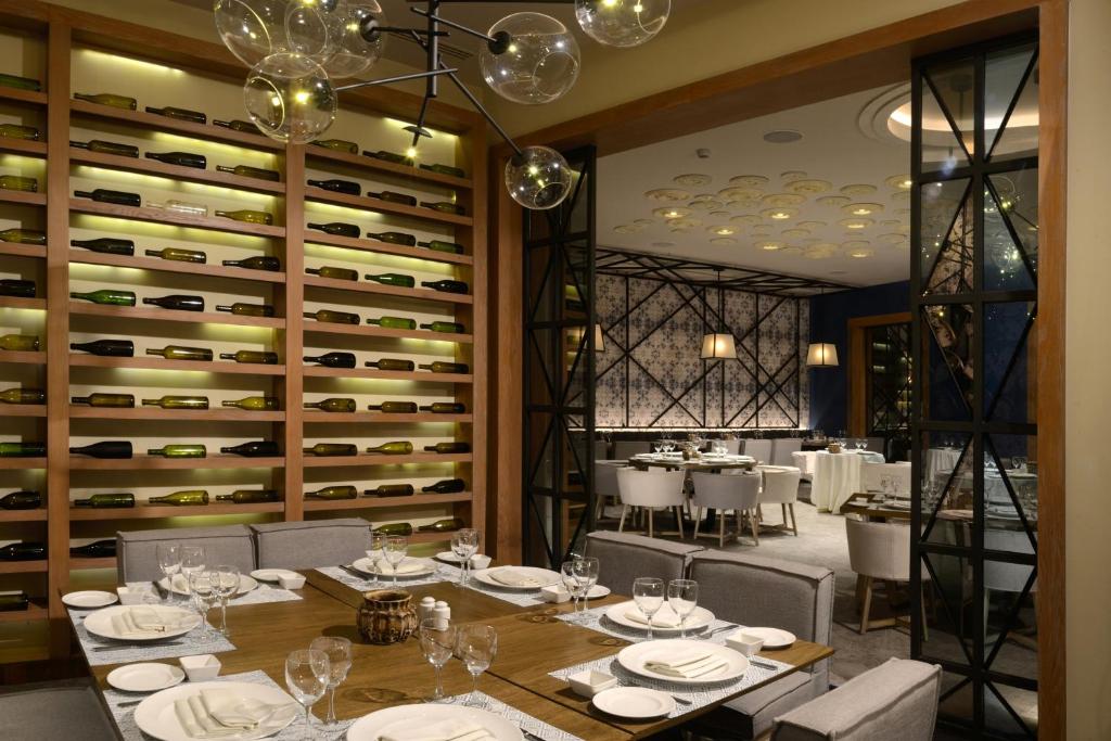 Elegants restorāns ar izsmalcinātu interjeru, kurā redzamas vīna pudeles un eleganti galdi ar galda piederumiem. Gaismas un dizains rada mājīgu atmosfēru.