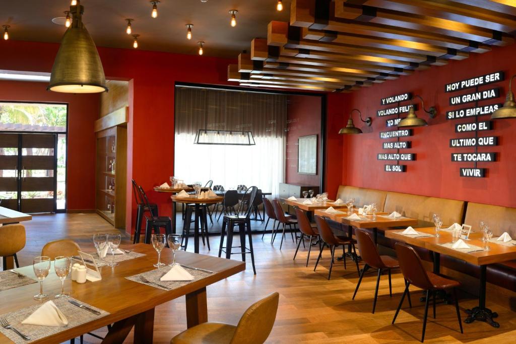 Mūsdienīga restorāna iekārtojums ar siltu apgaismojumu, koka elementiem un sarkaniem sienām. Galdi ir elegantā izkārtojumā, gatavi viesu uzņemšanai.