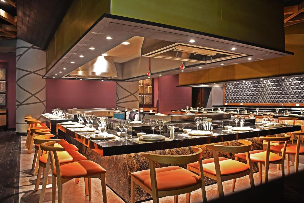 Mūsdienīgs restorāns ar elegantu interjeru, kurā redzams garšīgs ēdamgaldu klājs un krāsainas krēsli. Izcelti moderni apgaismojumi un stilīgs virtuves dizains.