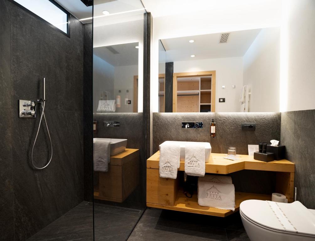 Mūsdienīga vannas istaba ar dušu, elegantu melnu akmens apdari un koka mēbelēm, kurās ir dvieļi un vannas piederumi. Iekārtota ar modernu apgaismojumu un spoguli.