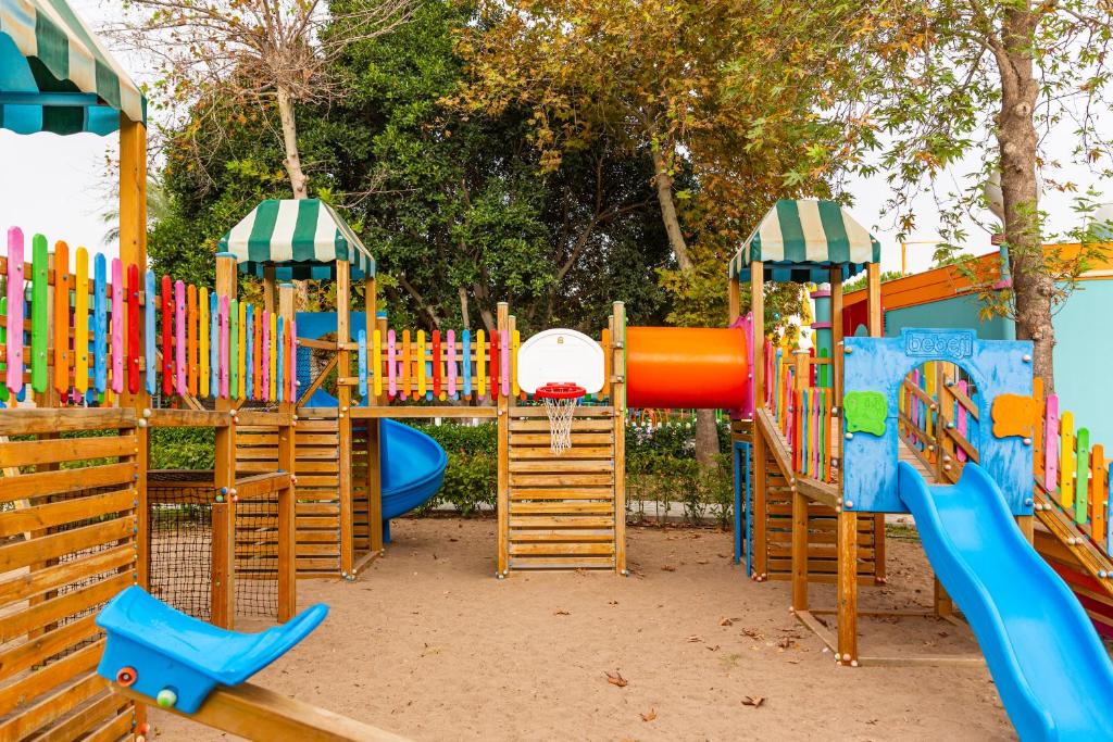 Krāsains bērnu rotaļu laukums ar slidkalniņiem, šūpolēm un tuneli, kas ieskauts zaļojošos kokus. Ideāla vieta bērnu spēlēm un izklaidei.