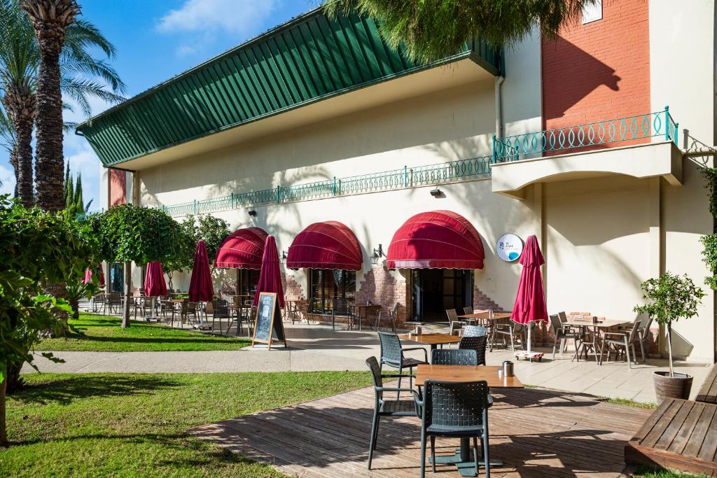 Āra kafejnīca ar sarkanām nojumi un koka terasi, apkārt palmām un zaļumiem. Ideāla vieta relaksācijai un atpūtai.