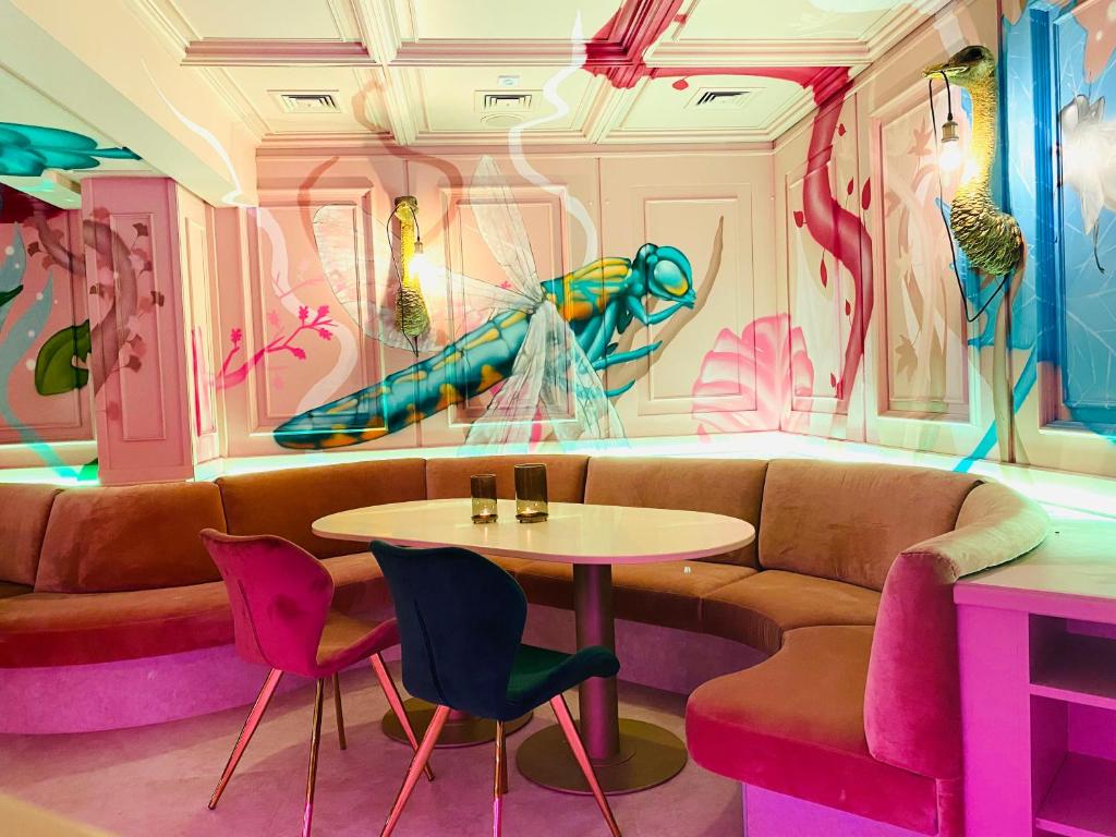 Moderns interjers ar krāsainām sienu gleznām, kas attēlo dabas elementus, un stilīgu apaļu galdu ar dīvānu.