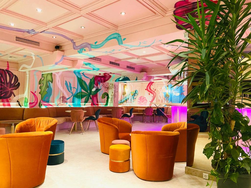 Krāsains interjers ar oranžām krēslām un augiem, izrotāts ar modernām sienu gleznām. Šī vieta rada relaksējošu un stilīgu atmosfēru.