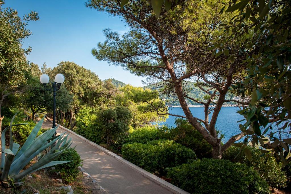 Pastaiga gar jūras krastu, ko ieskauj zaļumi un koki, ar gaismas stabu, kas piešķir idillisku atmosfēru.