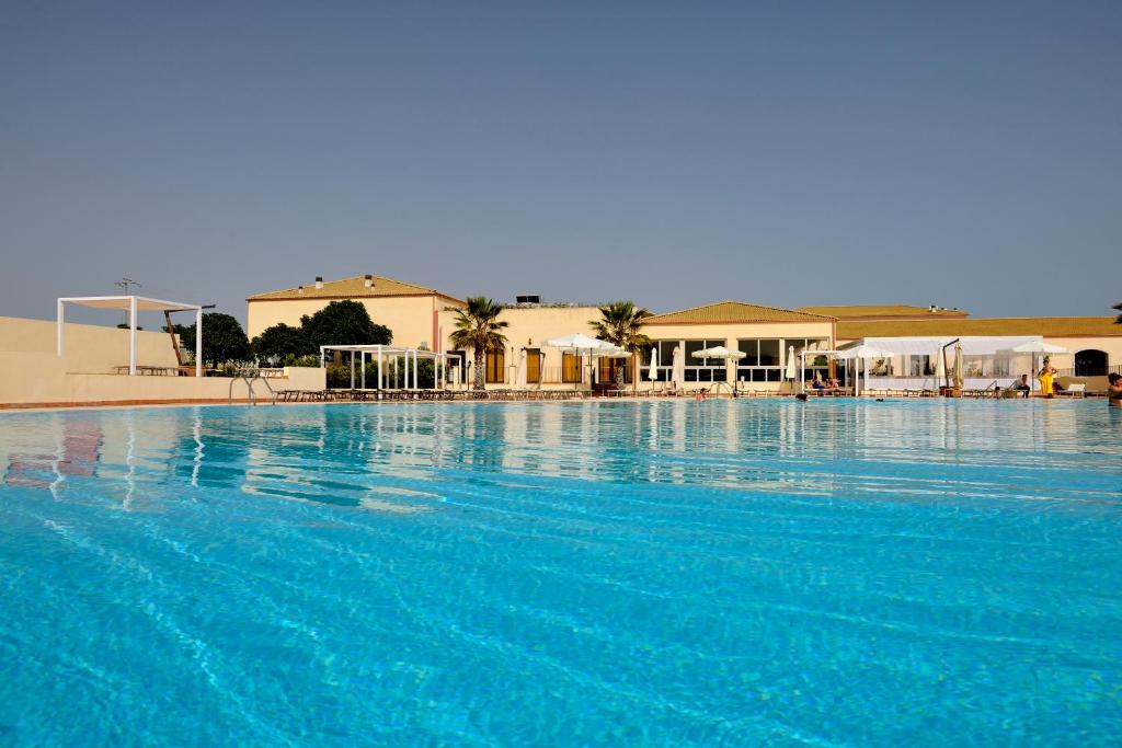 Liels, skaidrs peldbaseins ar zilu ūdeni un viesnīcu fona, apkārt palmām un atpūtas zonām. Ideāla vieta relaksācijai un atpūtai saulainā dienā.