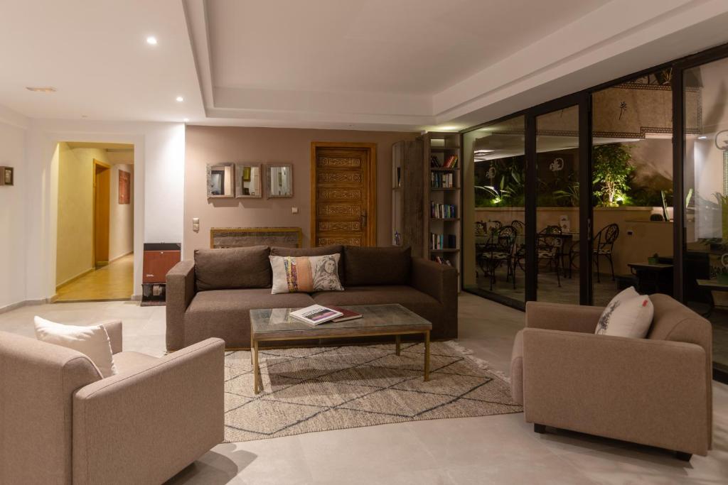 Mūsdienīgs viesistabas interjers ar ērtām dīvāniem, galdu un piekļuvi dārzam caur liela stikla sienu. Telpa ir gaiša un gaumīga, ar siltām krāsām un dekoratīviem elementiem.