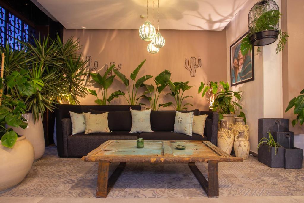 Mūsdienīgs viesistabas interjers ar tumšu dīvānu, dekoratīvām spilvendrānām un koka galdu, apņemts ar zaļām telpaugiem un siltu apgaismojumu. Detaļas ar mākslas darbiem un keramikas traukiem piešķir telpai unikālu raksturu.