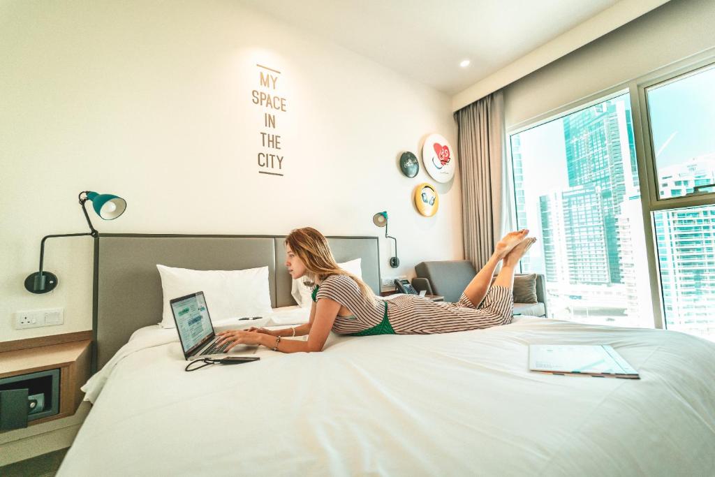 Sieviete strādā viesnīcas Rove Dubai Marina numurā ar skatu uz pilsētu.