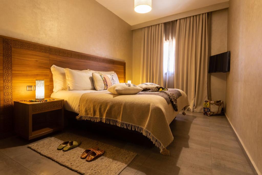 Mūsdienīgs guļamistabas interjers ar ērtu gultu, siltu apgaismojumu un televizoru. Uz grīdas redzamas čības, bet pie gultas atrodas naktsgaldiņš ar dekoratīvu lampu.