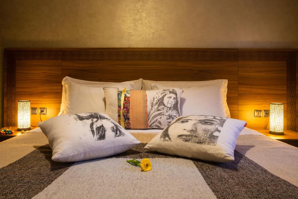 Mūsdienīga guļamistaba ar koka gultas galvgali, dekoratīviem spilveniem un siltu apgaismojumu. Gultas veļa ir eleganta un mājīga, radot relaksējošu atmosfēru.