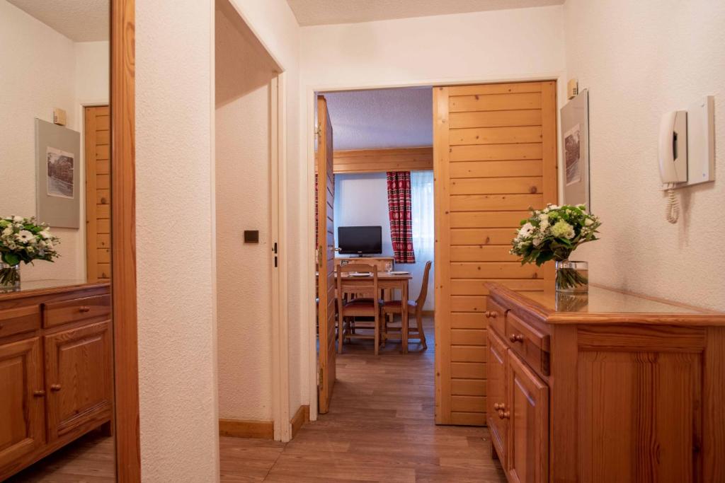 Gara koridora ar koka mēbelēm, kurā redzams galds un televizors, kā arī ziedi uz konsoles. Interjers ir gaišs un viesmīlīgs.