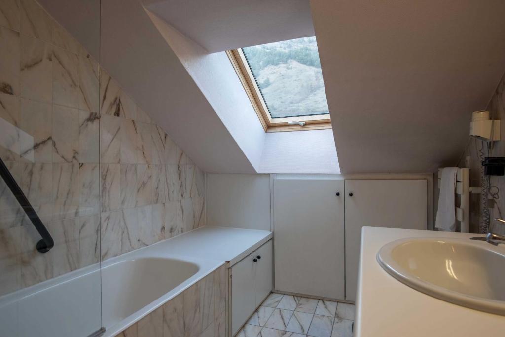 Mūsdienīgs vannas istabas interjers ar akmens apdari, logu uz jumta un vannu. Telpa ir gaiša un funkcionāla, radot relaksējošu atmosfēru.