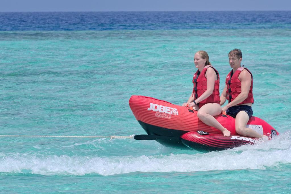 Divi cilvēki izklaidējas uz sarkana ūdens motocikla, braucot pa tirkīza jūru, vilkšanas laikā izskatās priecīgi un droši.