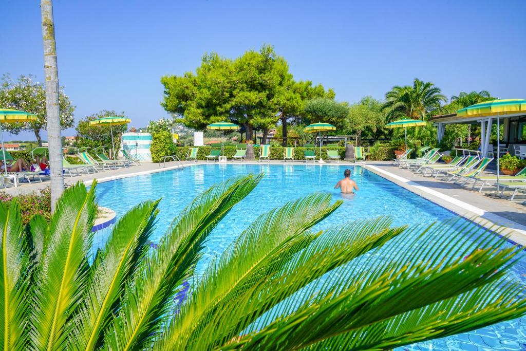 Peldbaseins ar sauļošanās krēsliem un zaļām parasolēm, ieskauts zaļumiem un palmām, rada relaksējošu atmosfēru. Ideāla vieta atpūtai un atvaļinājumam.