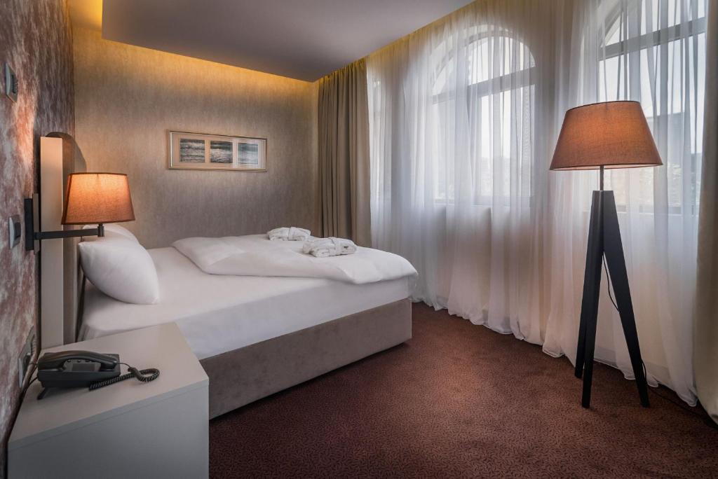 Mūsdienīga guļamistaba ar ērto gultu, stilīgu lampu un lieliem logiem, caur kuriem ieplūst dabiska gaisma. Interjers ir elegants un harmonisks, radot mierīgu atmosfēru.