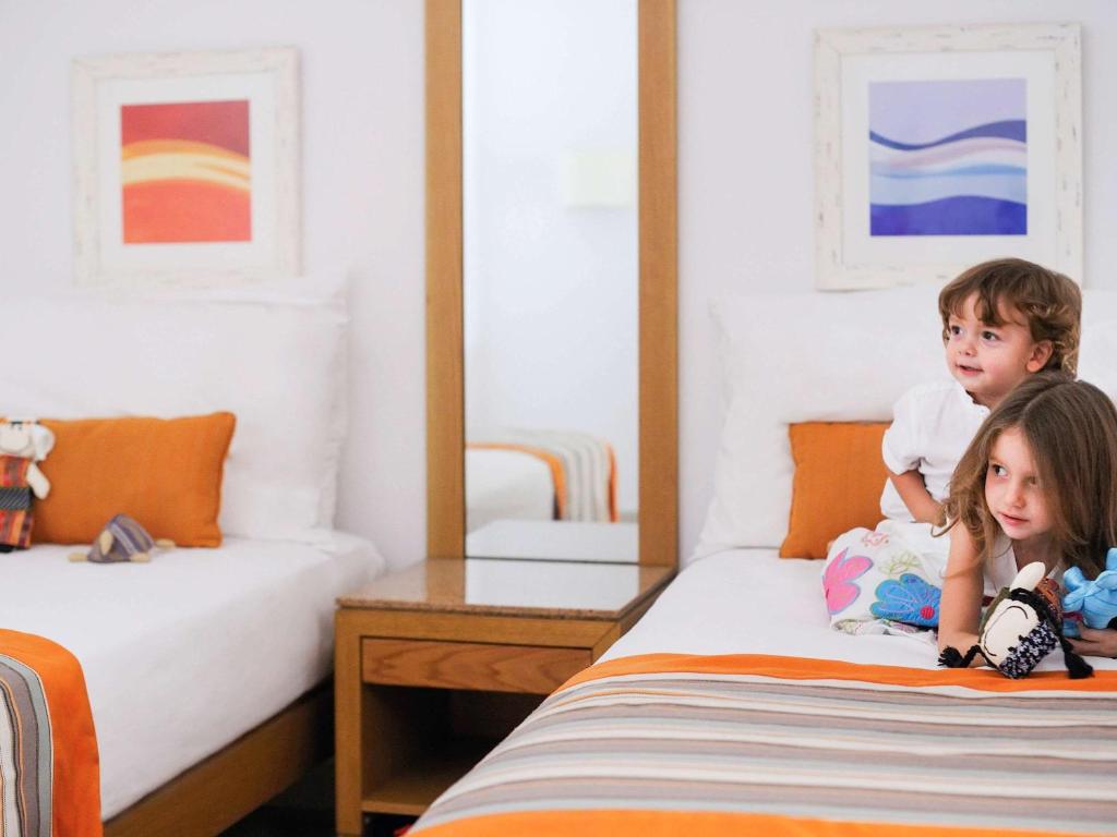 Divas bērnu istabā, spēlējoties uz gultas ar spilgtu gultas veļu un dekoratīviem elementiem. Iekārtojums ar modernu interjeru un lielu spoguli.