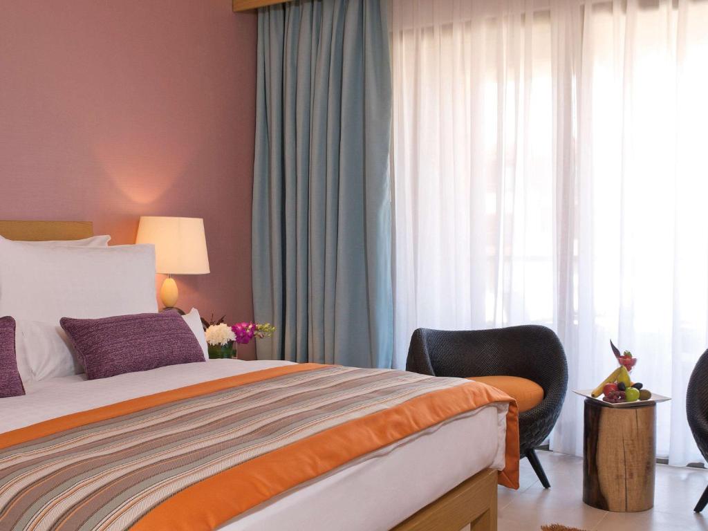 Mūsdienīga guļamistaba ar siltām krāsām, ērtu gultu un stilīgu atpūtas krēslu, kas papildināta ar augļu dekorāciju un dabīgu apgaismojumu.