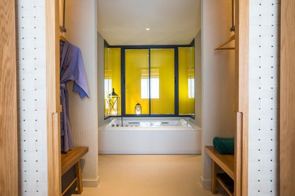 Mūsdienīgs vannas istabas interjers ar dzeltenu stiklu, koka mēbelēm un relaksējošu atmosfēru. Svaigi sagatavoti dvieļi un halāti pieejami ērtiem spa mirkļiem.