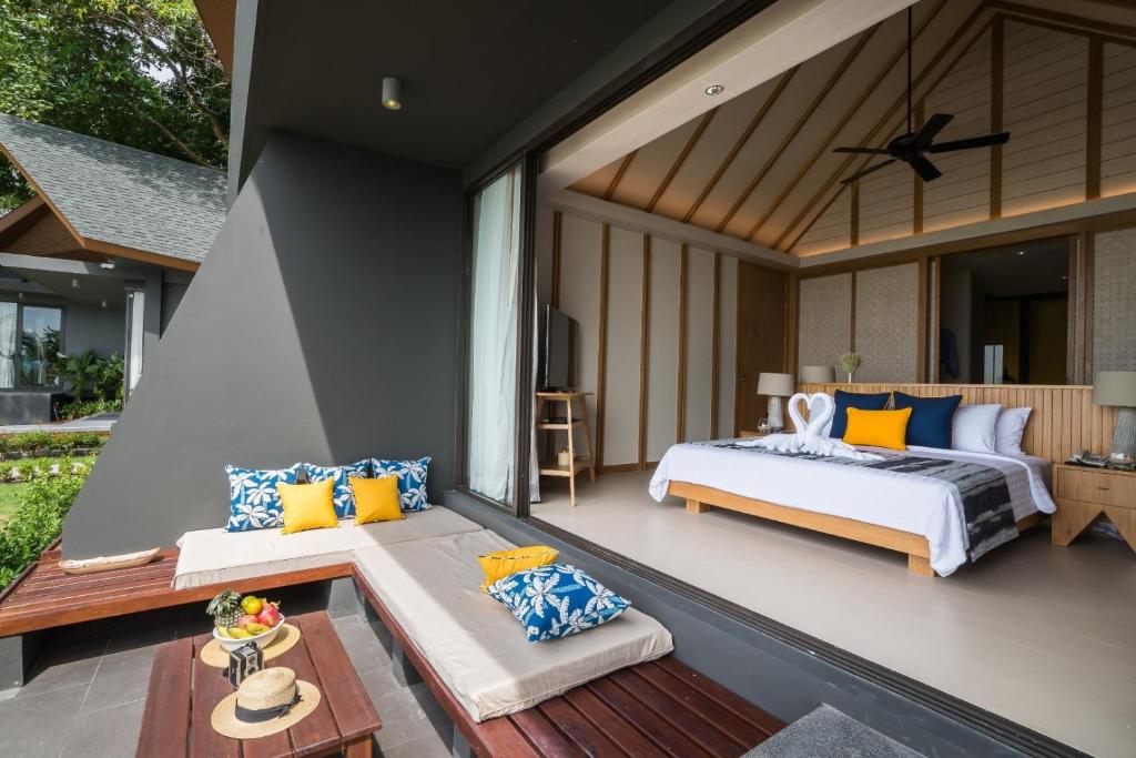 Mūsdienīgs guļamistabas interjers ar plašām stikla durvīm, kas ved uz ārējo terasi, kur atrodas ērti spilveni un augļu komplekts. Telpa ir gaiša un gaumīgi iekārtota, ar mūsdienīgu dizainu un dabīgu apgaismojumu.