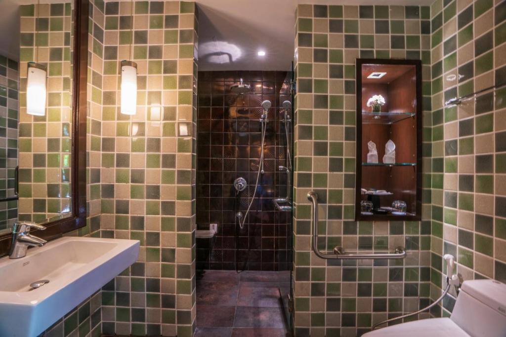 Mūsdienīga vannas istaba ar zaļiem un pelēkiem flīzēm, elegantu izlietni un dušu, kas aprīkota ar divām dušas galvām. Interjers ir apgaismots ar modernām gaismām un dekorēts ar stikliem.