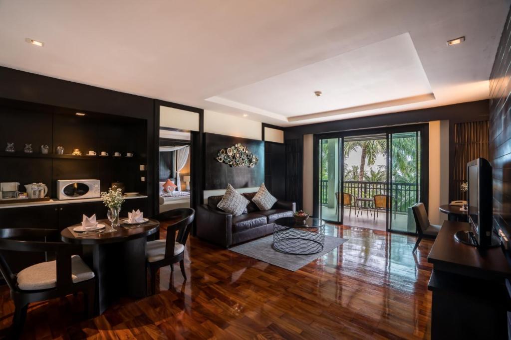 Mūsdienīgs viesnīcas numurs ar elegantu interjeru, ērtu dīvānu un ēdamgaldu, kas piedāvā skatu uz balkonu ar tropisku ainavu. Gaismas un koka elementi rada siltu un mājīgu atmosfēru.