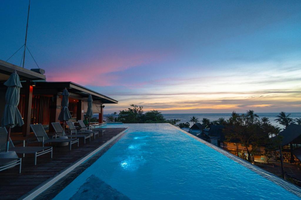 Peldbaseins ar panorāmas skatu uz jūru un krāšņu saulrietu, ap kuru ir atpūtas krēsli. Mūsdienīga arhitektūra un relaksējoša atmosfēra.